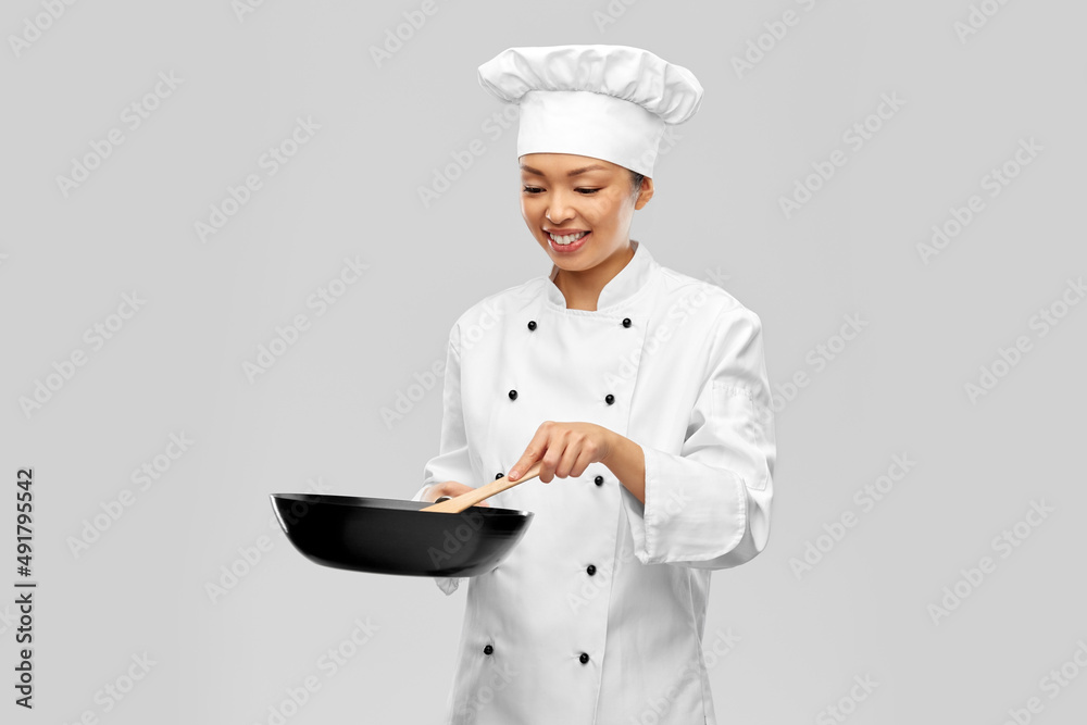 food cooking, culinary and people concept - happy smiling female chef in toque with frying pan and wooden spatula over grey background food cooking, culinary and people concept - happy smiling female chef in toque with frying pan and wooden spatula over grey background