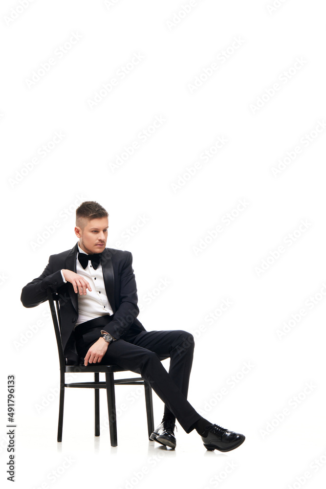 handsome man in tuxedo sitting on chair handsome man in tuxedo sitting on chair