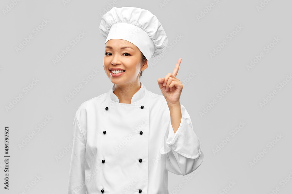 cooking, advertisement and food concept - happy smiling female chef in jacket pointing finger up over grey background cooking, advertisement and food concept - happy smiling female chef in jacket pointing finger up over grey background