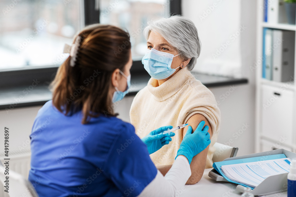 Obraz premium medicine, health and vaccination concept - doctor or nurse with syringe making vaccine or drug injection to senior woman in mask at hospital