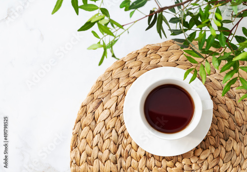 A cup of tea on a light marble background with green branches close-up. Spring women's concept. Top view and copy space