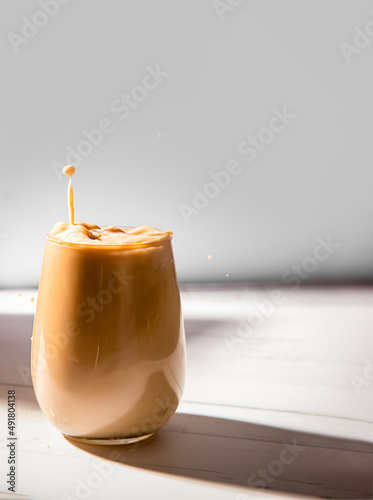 iced or frozen coffee in a glass, splash with drops, over grey background
