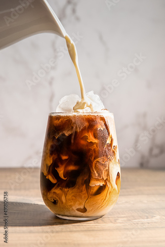 iced or frozen coffee in a glass, splash with drops, over grey background