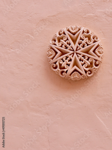 Detailed stucco heraldic emblem of Malta on rough painted wall of pastel colour. Vertical photo photo