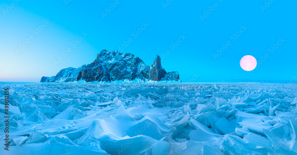 Beautiful winter landscape of frozen Lake Baikal at sunrise with full moon - Snowy ice hummocks with transparent blue piles of ice - Baikal Lake, Siberia