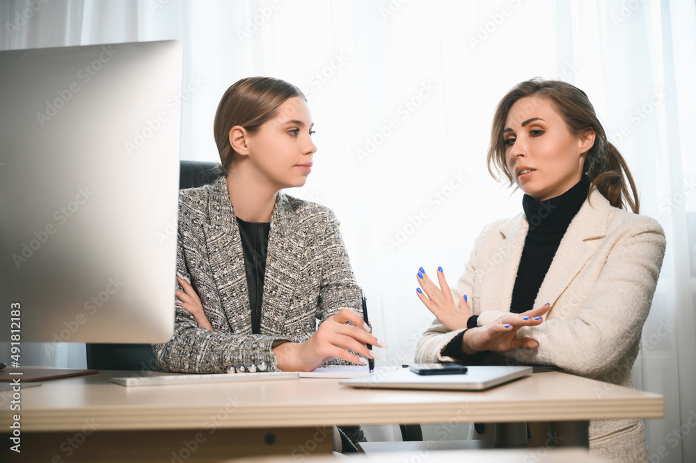 Attractive young adult women work together in the office at a meeting. A new employee consults with a mentor and presents a new project. Open space concept for teamwork Attractive young adult women work together in the office at a meeting. A new employee consults with a mentor and presents a new project. Open space concept for teamwork