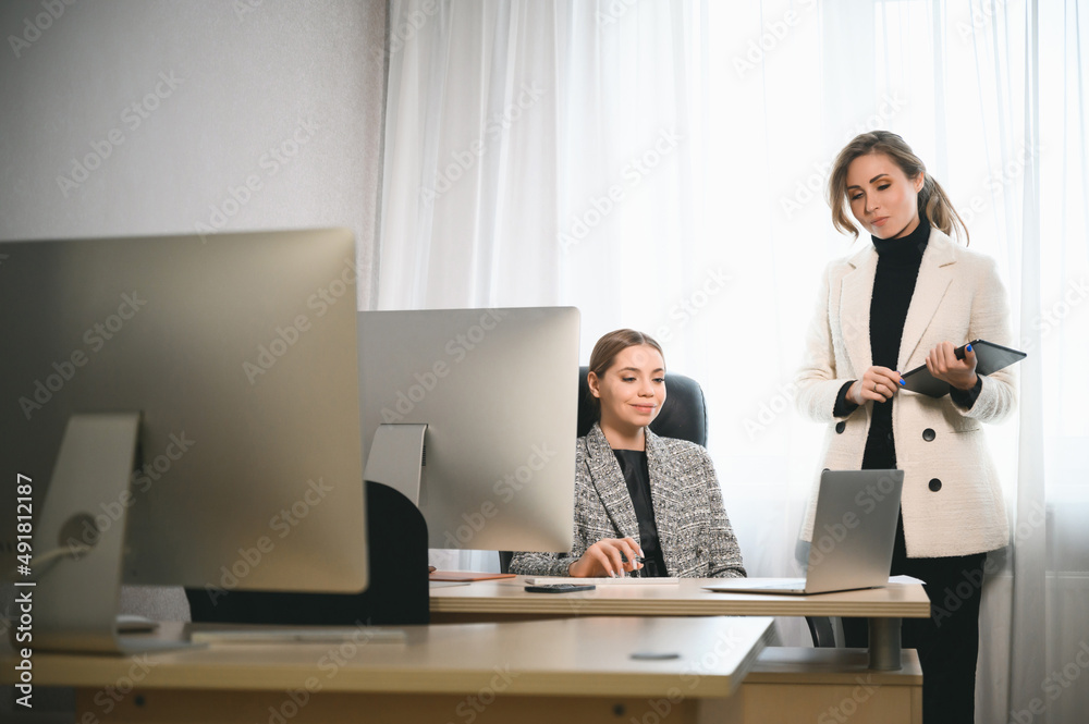 Attractive young adult women work together in the office at a meeting. A new employee consults with a mentor and presents a new project. Open space concept for teamwork Attractive young adult women work together in the office at a meeting. A new employee consults with a mentor and presents a new project. Open space concept for teamwork
