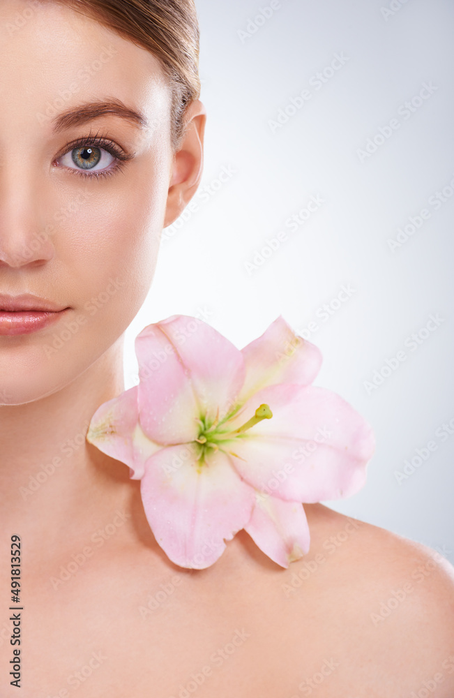 Floral beauty. Cropped studio portrait of half of a models face with a flower on her bare shoulder. Floral beauty. Cropped studio portrait of half of a models face with a flower on her bare shoulder.