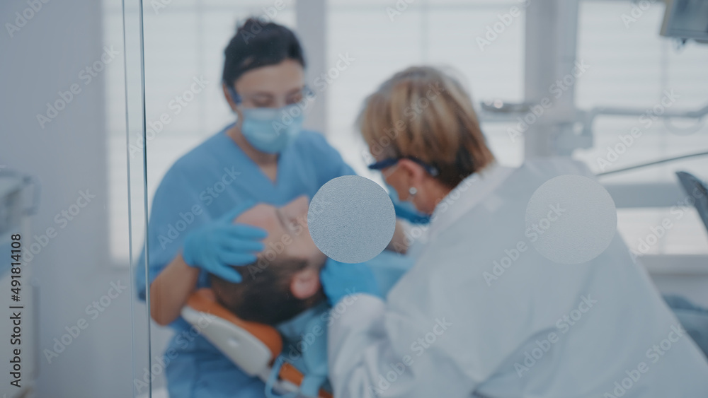 Fototapeta premium Team of experts performing oral care procedure with drill instrument in stomatology office. Orthodontist and assistant using dental tools and equipment at consultation with patient.