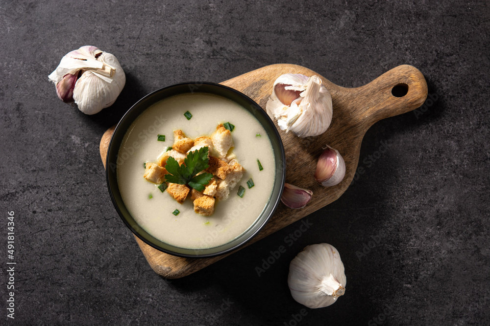 Garlic soup topped with croutons in bowl on black background - obrazy, fototapety, plakaty 