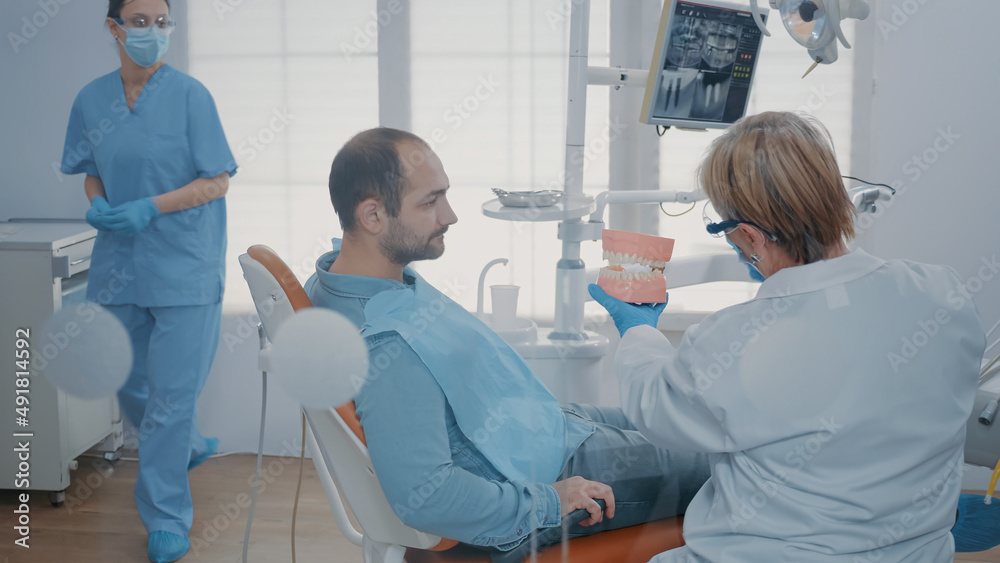 Obraz premium Dentist giving hygiene lesson to patient to clean teeth correctly with toothbrush and toothpaste in stomatology office. Expert showing oral care routine on artificial jaw to prevent caries.