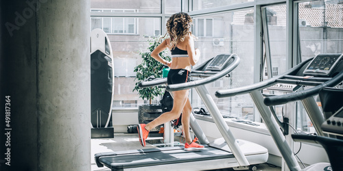 Attractive muscular smiling fitness woman running on treadmill in gym