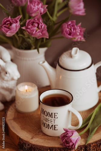 Still-life. A vase with flowers, tulips, a teapot, a bunny, a candle and a cup of tea on the coffee table in the living room home interior. Cozy spring concept.