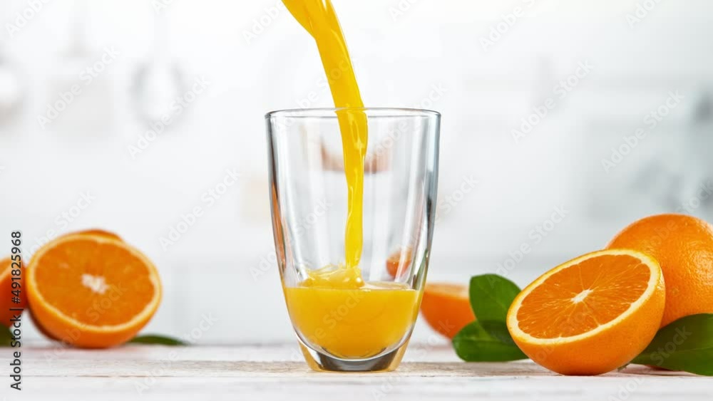 Super slow motion of pouring orange juice into glass. Placed on white table with kitchen interior. Filmed on high speed cinema camera, 1000 fps. Super slow motion of pouring orange juice into glass. Placed on white table with kitchen interior. Filmed on high speed cinema camera, 1000 fps.