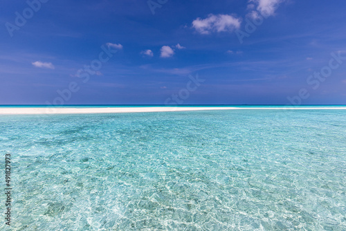 Closeup sandy beach waves and blue summer sky. Panoramic beach landscape. Empty tropical beach and seascape. Bright blue sky, soft sand, calmness, tranquil relaxing sunlight, summer mood