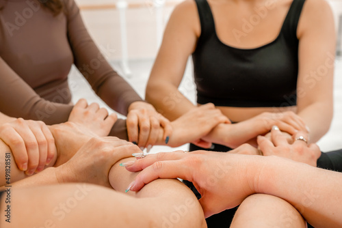 Partnership and unity concept: unrecognizable women in sportswear holding wrists of each other, forming circle. Group of happy young women holding hands. Side view on human hands.