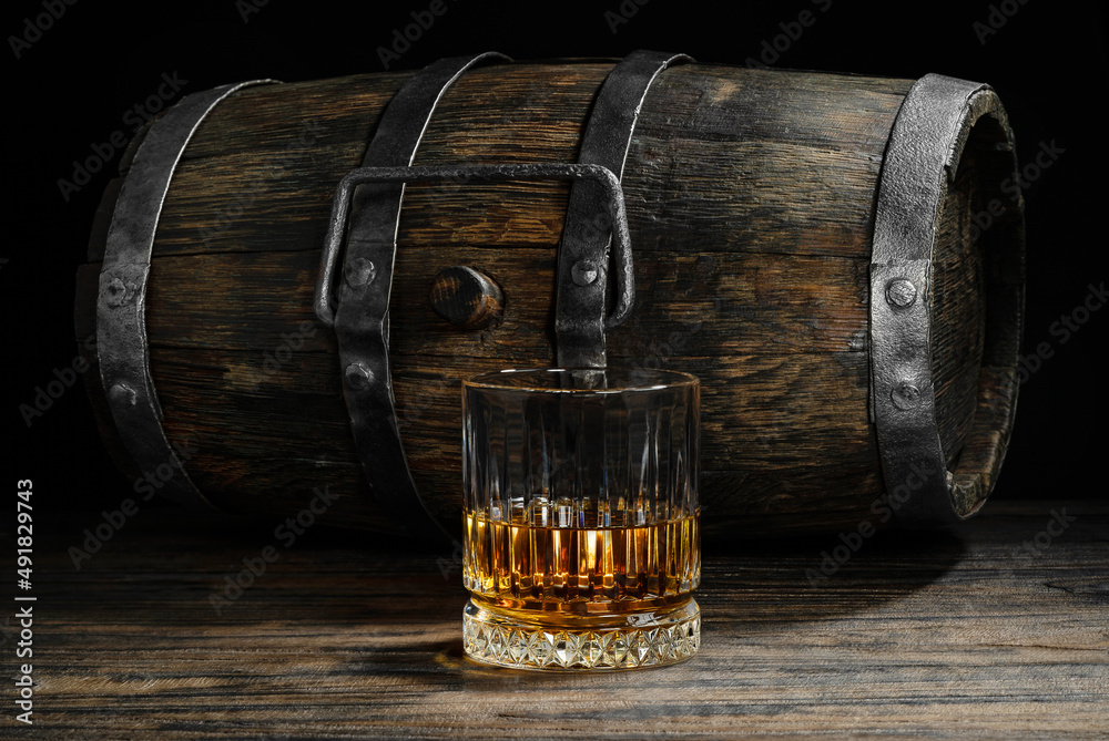 Aged scotch whiskey and old wooden keg on dark background