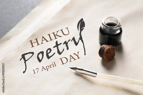 Paper sheet with text HAIKU POETRY DAY 17 APRIL and feather pen with inkwell on table, closeup photo