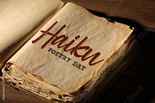 Photos Open old book with text HAIKU POETRY DAY on wooden background