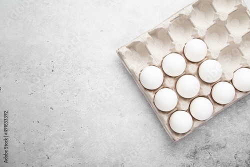 White chicken eggs in paper tray on light background. Concept farm products and natural nutrition. Top view, copy space or empty place for text.