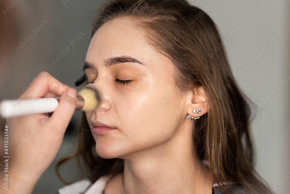 Makeup artist distributes foundation on the girl's face with a brush Makeup artist distributes foundation on the girl's face with a brush
