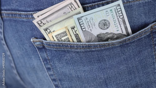 man putting a pack of dollar currency cash banknotes in the back pocket of blue jeans close-up. concept of rising price or financial success