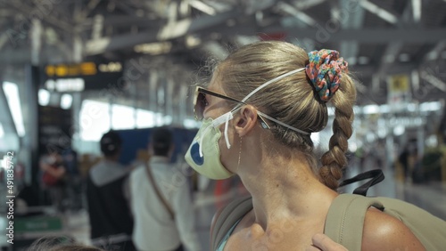 Woman caucasian at Suvarnabhumi Airport with wearing protective medical mask on head against background of plane. Concept health virus protection coronavirus epidemic sars-cov-2 covid-19 2019-ncov. © ivandanru