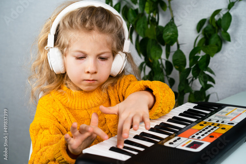 a little blonde girl in headphones smiling and playing the synthesizer, the concept of teaching children music © Надежда Урюпина