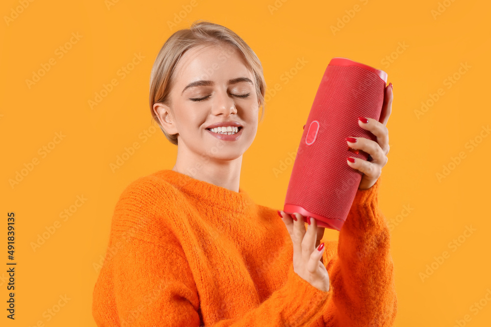 Smiling woman with closed eyes holding modern wireless portable speaker on color background Smiling woman with closed eyes holding modern wireless portable speaker on color background