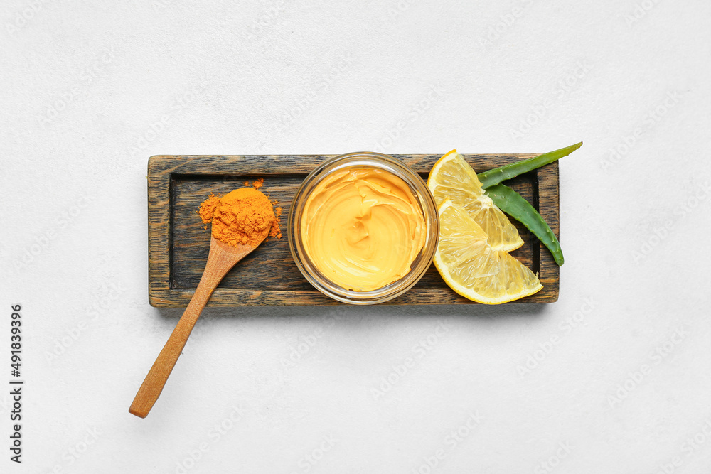Wooden board with jar of turmeric mask, powder, lemon and aloe on light background Wooden board with jar of turmeric mask, powder, lemon and aloe on light background