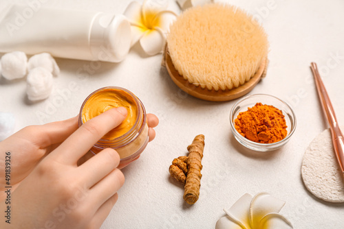 Woman trying turmeric mask in jar on light background