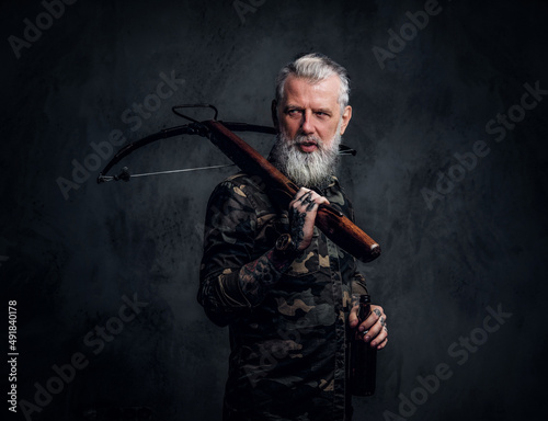 Leinwand Poster Bearded old man with grey hairs holding crossbow on his shoulder