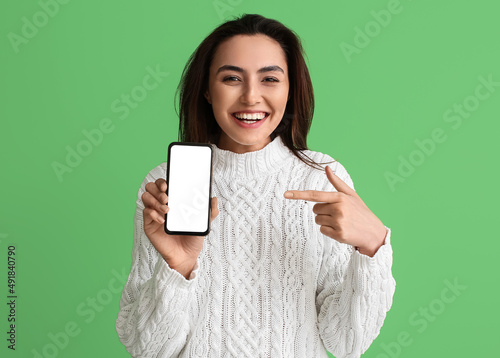 Smiling woman pointing at mobile phone with blank screen on green background. E-mail concept