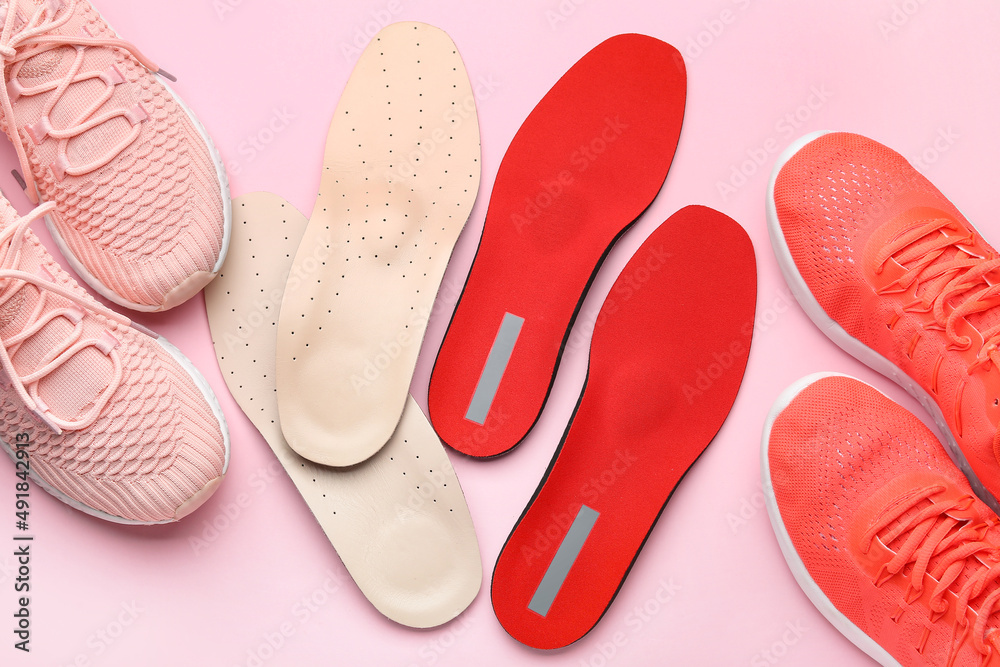 Fototapeta premium Orthopedic insoles and sportive shoes on pink background, closeup