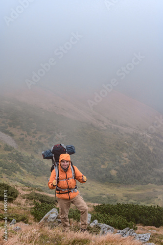 A man climbs a mountain in the fog, a man carries a backpack on his back.