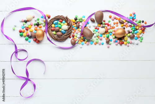 Composition with chocolate Easter eggs and different candies on light wooden background