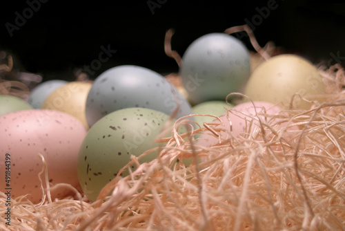 Easter eggs in straw nest decoration – extreme close-up, full frame, abstract, image focus technique of colorful, pastel speckled Easter eggs in fluffy straw nest basket, background texture
