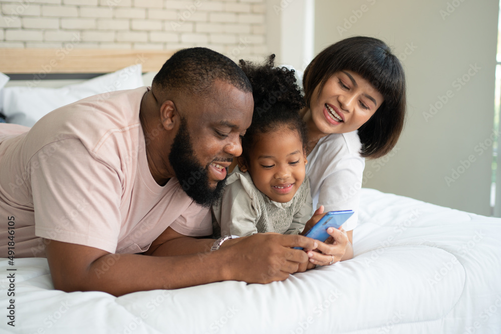 The family has fun and plays education games online with a smartphone at home in the bedroom. Concept of online education and caring from parents. The family has fun and plays education games online with a smartphone at home in the bedroom. Concept of online education and caring from parents.