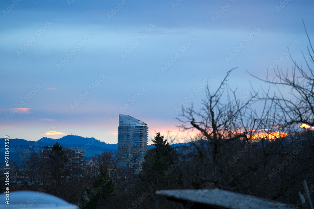 Scenic colorful sky at sunrise on a cloudy winter day at Zürich Schwamendingen with tree in the foreground and skyscraper in the background. Photo taken February 18th, 2022, Zurich, Switzerland. Scenic colorful sky at sunrise on a cloudy winter day at Zürich Schwamendingen with tree in the foreground and skyscraper in the background. Photo taken February 18th, 2022, Zurich, Switzerland.