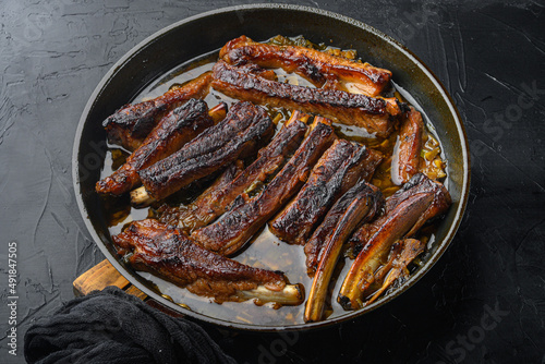 Grilled pork rib, in frying cast iron pan, on black stone background
