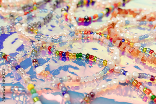 Closeup of necklaces and bracelets made from colorful beads and pearls on a pink holographic background.