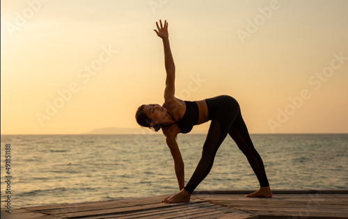 Silhouette of woman practicing yoga on a coastal wooden bridge during sunset.