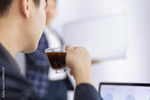 Business partners concept a young male entrepreneur holding a cup of black coffee sitting with a laptop while attending in a monthly meeting