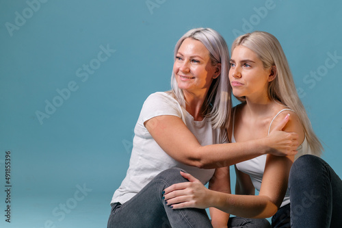 Blondehaired Mom and teenager daughter smiling on colorful backgroung. studio shoot with copy space photo