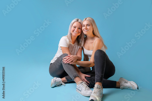 Blondehaired Mom and teenager daughter smiling on colorful backgroung. studio shoot with copy space photo