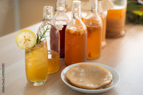 Kombu tea in a glass with ice, lemon slices and rosemary leaves, Homemade fermented raw kombucha tea in bottles and glass jars mix with fruit juice and scoby on table.Healthy natural probiotic drink. photo