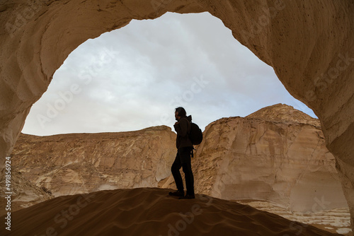 El Aqabat valley in the White Desert, Egypt - January 2022: Young man standing under the arch of rock formations