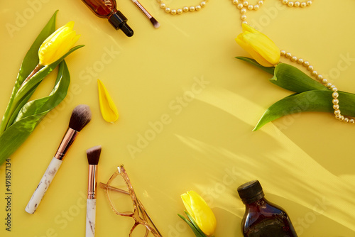 Yellow vivid feminine flat lay: makeup brushes, glasses, oil, serum dropper, pearls. Yellow tulips with trendy shadows. Beauty card concept. Copy space. photo