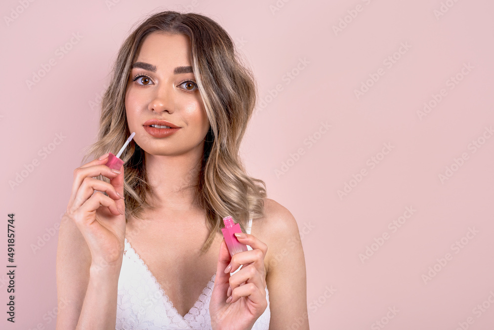 Beutiful blonde girl with natural makeup on light pink background, holding a lipstick , copy space Beutiful blonde girl with natural makeup on light pink background, holding a lipstick , copy space