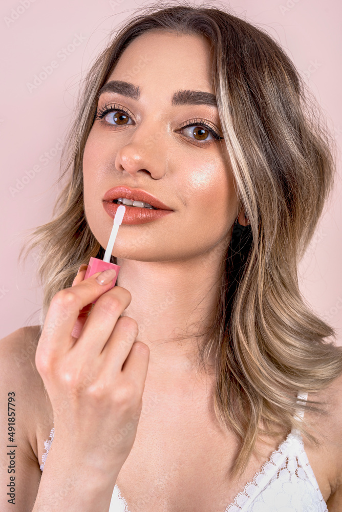 Beutiful blonde girl with natural makeup on light pink background, holding a lipstick , copy space Beutiful blonde girl with natural makeup on light pink background, holding a lipstick , copy space